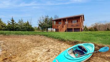 A wooden cabin with a balcony, a kayak, and a paddle on the ground.