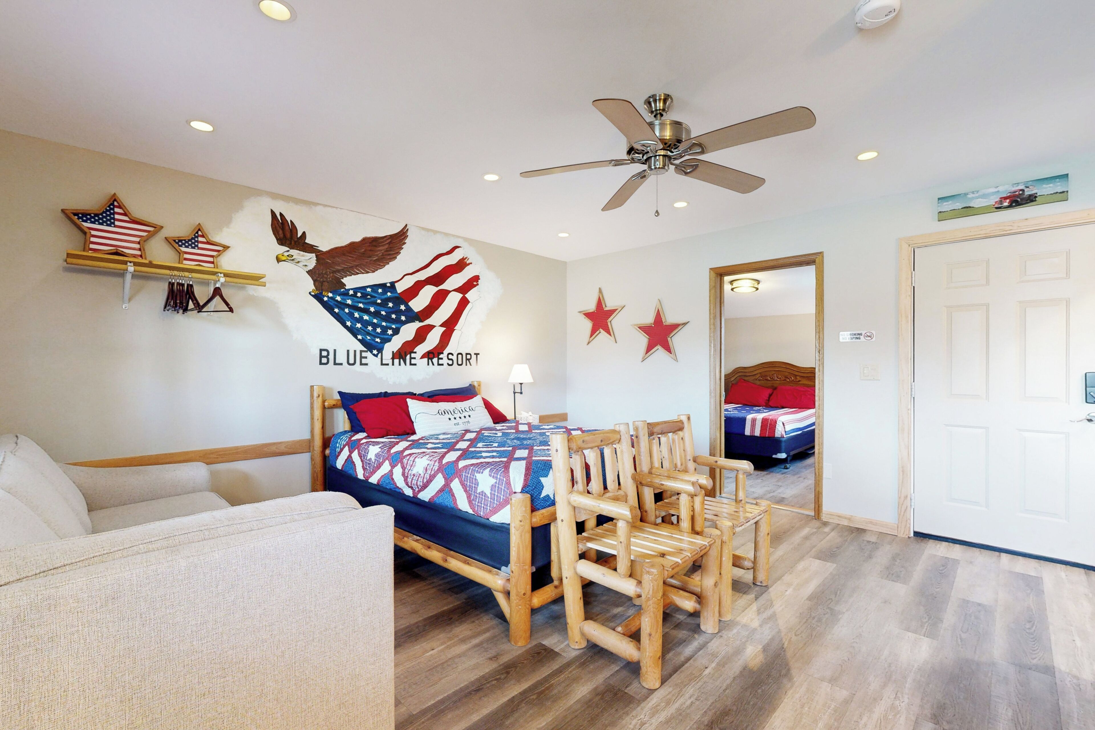 Une chambre à coucher avec un lit, des chaises en bois, un ventilateur de plafond et une fresque murale représentant un aigle et des étoiles.