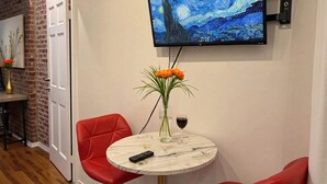A room with a round table, red chairs, a TV displaying a painting, a vase with flowers, and a wine glass. - Sunny 1BR in Heart of Hell's Kitchen (New York)
