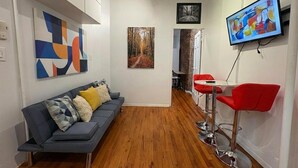 A modern living space with a sofa, red chairs, a TV, and artwork on the walls. - Sunny 1BR in Heart of Hell's Kitchen (New York)