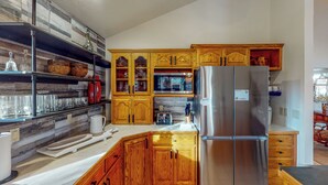 A modern kitchen with wooden cabinets, a stainless steel refrigerator, and a built-in microwave. - Work & Play! Spacious Lake-View Home in Greeley (Greeley)