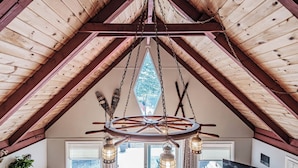 A rustic interior with a wooden ceiling, a large circular wooden wheel chandelier, and a television on the wall. - Dock! Dog-Friendly Lakefront Gem in Southern Maine (Waterboro)