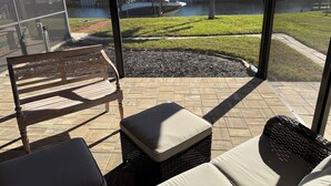 A patio with a bench, a wicker chair, and a cushioned ottoman. - Gorgeous 3-bedroom pool, Direct gulf access In SE Cape Coral. Close to downtown (Cape Coral)