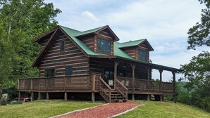 Une cabane en rondins avec un toit végétalisé, une véranda et un chemin recouvert de paillis rouge menant à l’entrée.