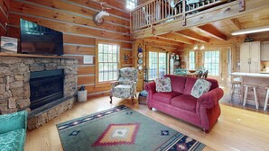 L’intérieur d’un chalet rustique, avec une cheminée en pierre, un canapé rouge, un coin repas en bois et une cuisine dotée de meubles en bois.