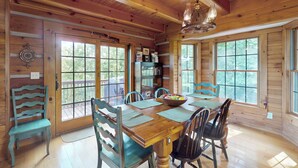 L’intérieur d’un chalet en bois, avec une table à manger, des chaises, un lustre et de grandes fenêtres.