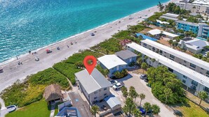 An aerial view of a coastal hotel with a beach, including a parking area, a pool, and a thatched-roof structure. - Island Breeze Condo on the Beach (Englewood)