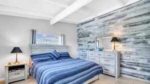 A bedroom with a bed, nightstand, dresser, and a wall with a textured design. - Island Breeze Condo on the Beach (Englewood)