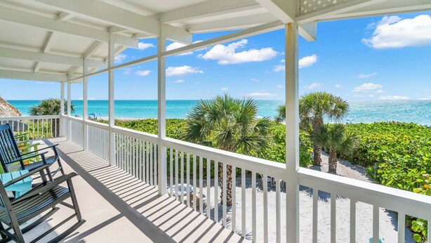 A covered balcony with white railings, overlooking a beach with palm trees and the ocean. - Island Breeze Condo on the Beach (Englewood)