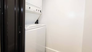 A compact, white laundry room with a built-in washer and dryer, a dark door, and a white wall. - Double King Studio 800sqft (Los Angeles)