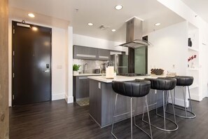 A modern kitchen with a central island, bar stools, and a dark wooden floor. - Double King Studio 800sqft (Los Angeles)
