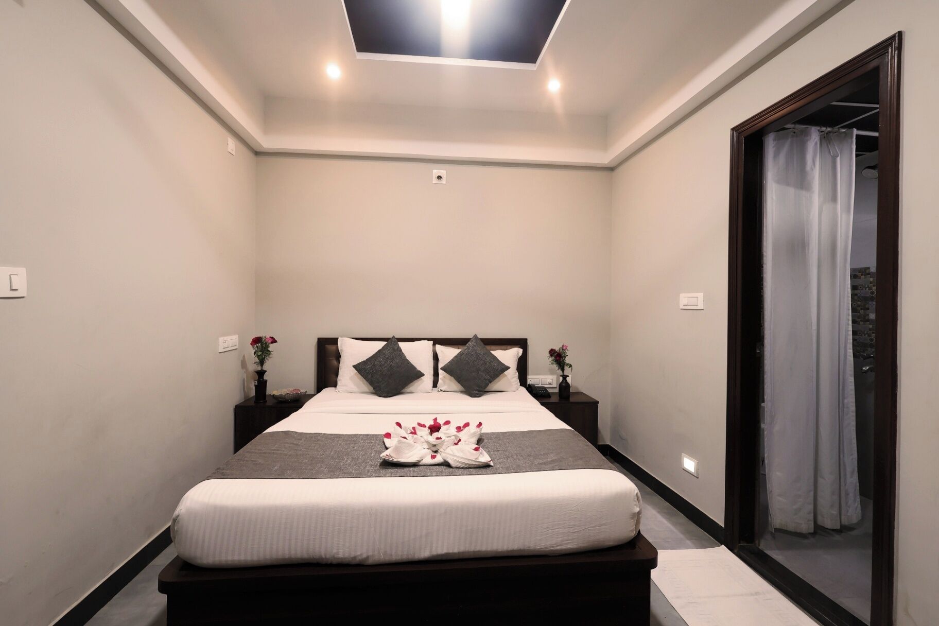 Un dormitorio moderno con una cama grande, cabecera oscura, mesitas de noche con jarrones y un tragaluz.