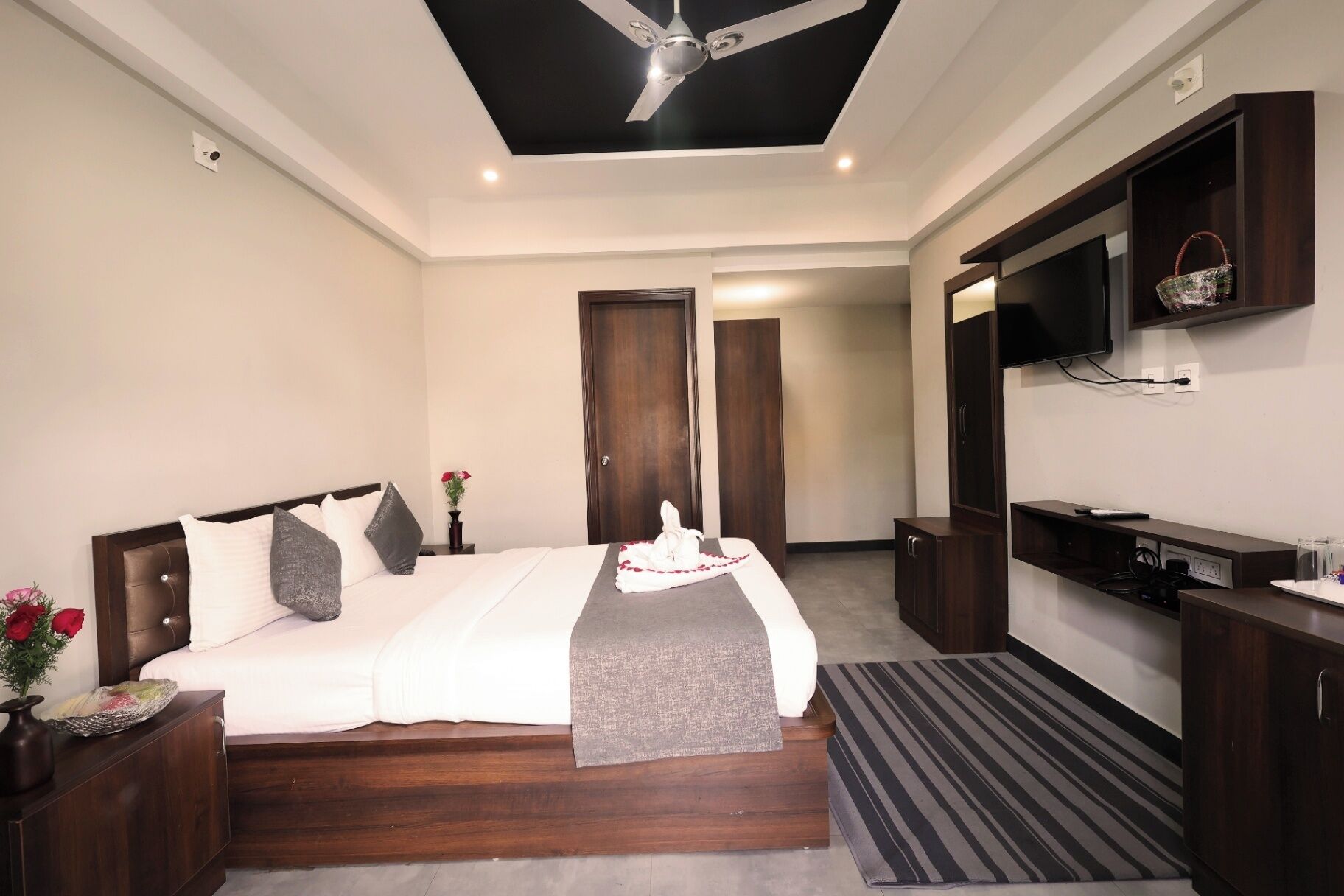 Una habitación de hotel con una cama, televisor, ventilador de techo y un escritorio pequeño.