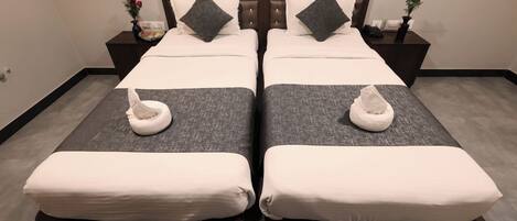 Una cama doble con dos almohadas, una mesita de noche con un florero y una toalla en cada cama.