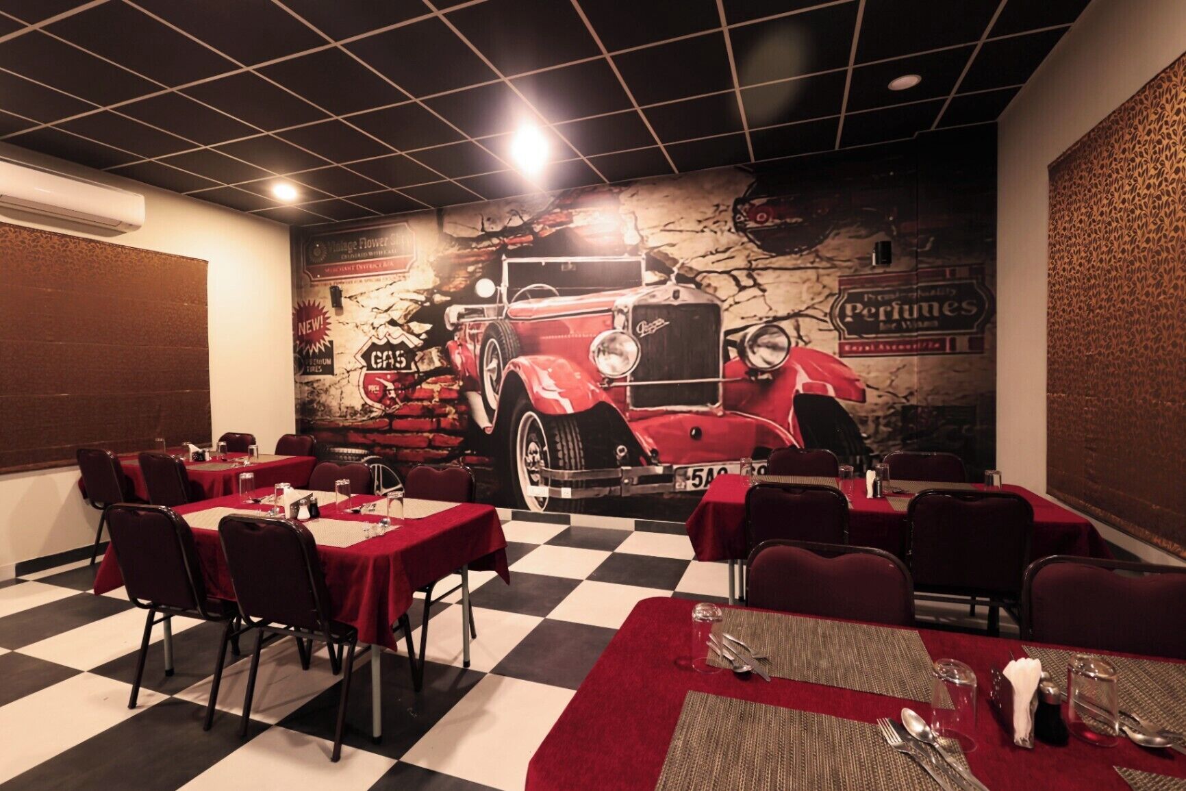 A restaurant with a vintage car mural, checkered floor, and red tablecloths.