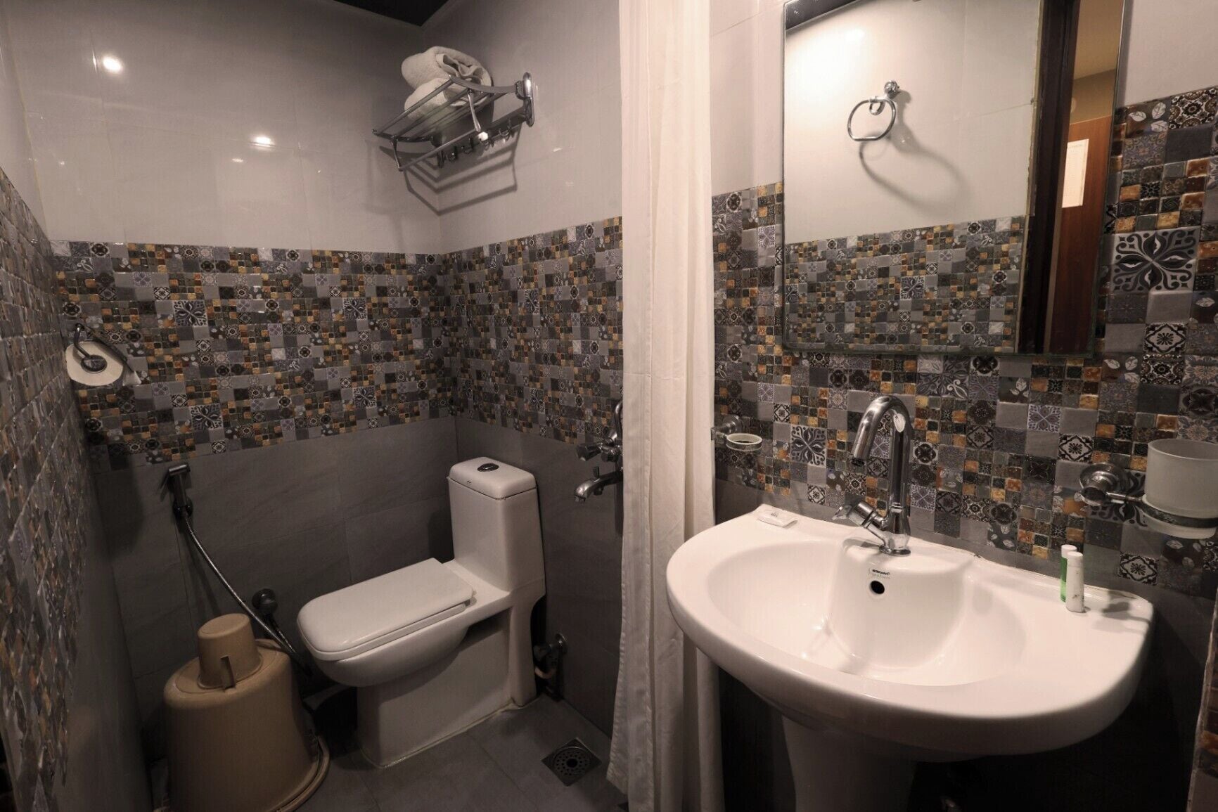 Baño con inodoro, lavamanos y ducha. Las paredes están revestidas con un diseño de mosaico.