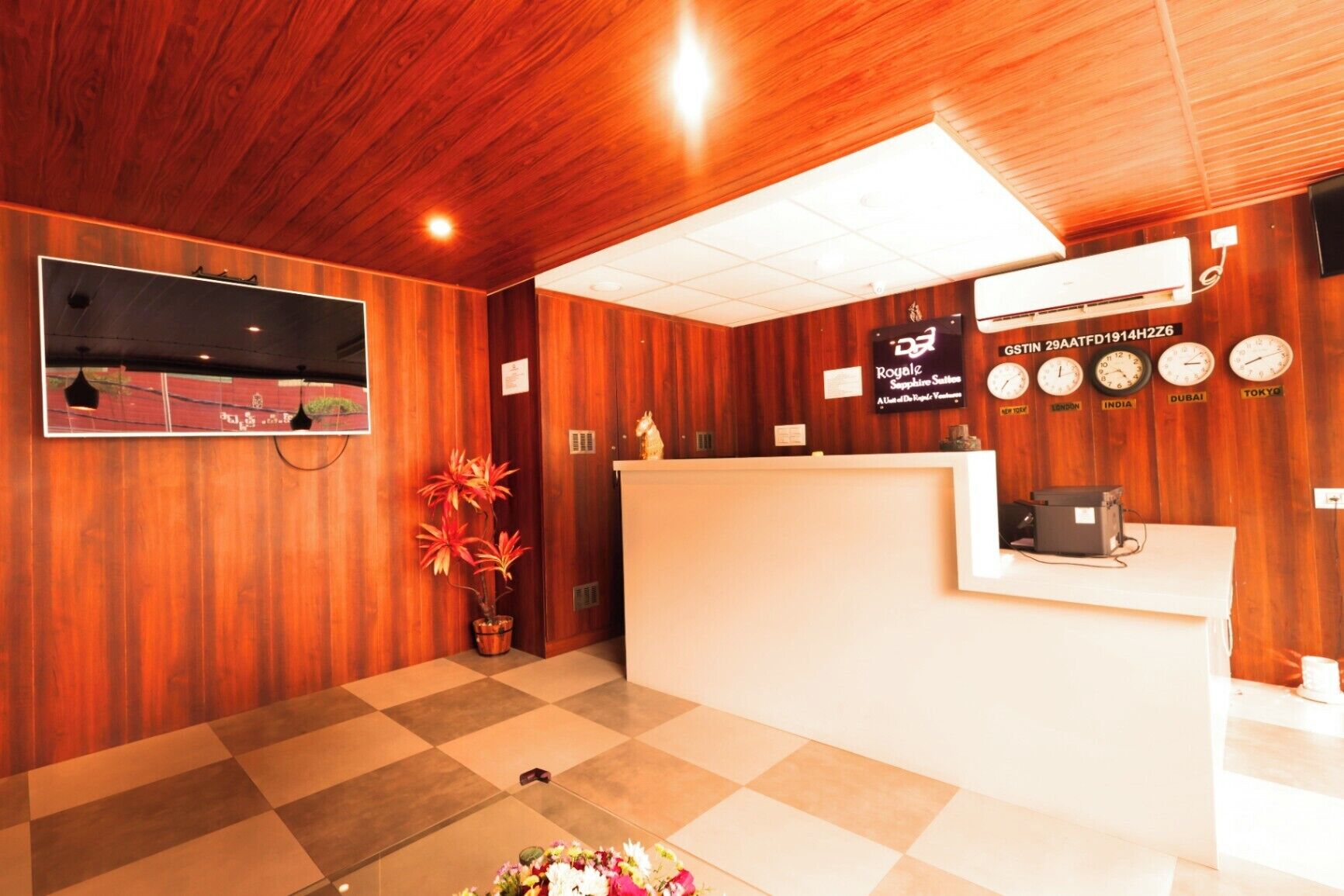 Een receptiezone met houten inrichting, een receptiebalie, een potplant, een klok en een wandairconditioner.