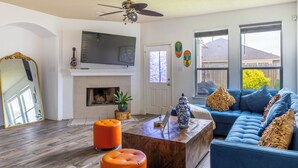 A living room with a fireplace, a blue sofa, orange ottomans, and a wooden coffee table. - Marvelous 5-bedroom house with AC in charming Tomball (Tomball)