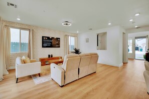Ein geräumiges Wohnzimmer mit einem beigefarbenen Sofa, einem weißen Sessel und einem Holztisch.