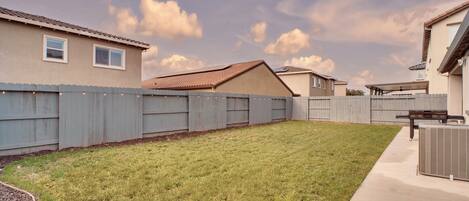 A residential backyard with a grassy lawn, a wooden fence, and a patio area with an air conditioning unit.