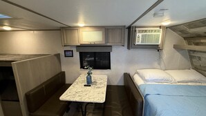 Un interno camper compatto con angolo cottura, un piccolo tavolo da pranzo, un letto e un'area salotto.