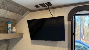 Un televisore montato su una parete strutturata, con una presa di corrente sopra e una finestra che mostra un'auto all'esterno.