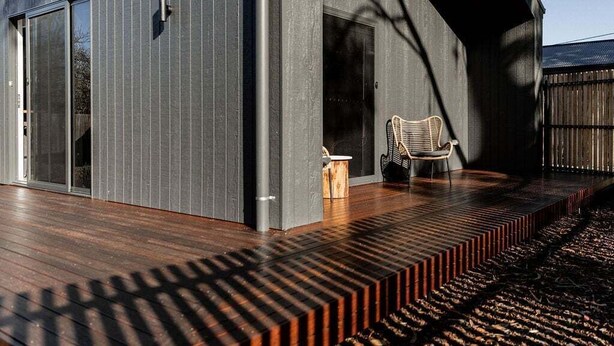 Um edifício moderno com um deck de madeira, uma cadeira e uma pequena mesa.