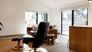Uma sala de estar moderna com uma poltrona preta, um sofá marrom, uma mesa de centro de madeira e uma mesinha redonda.