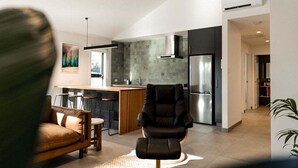 Cozinha moderna com ilha central, área de refeições com sofá de couro e uma cadeira preta.