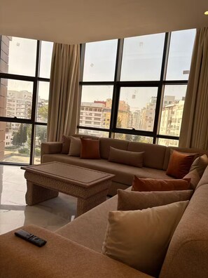 Amplia sala de estar con un gran ventanal, un conjunto de sofás y una mesa de centro tejida.