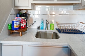 Una cucina con un lavandino in acciaio inossidabile, un tagliere di legno e diversi alimenti e utensili da cucina.