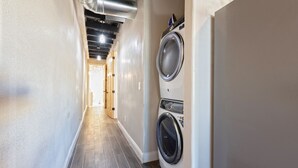 A laundry room with a washing machine and dryer, a tiled floor, and a hallway leading to another room.
