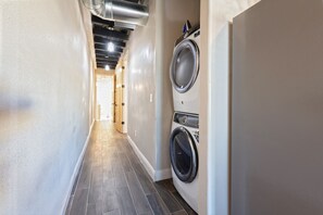 Une buanderie équipée d’un lave-linge et d’un sèche-linge, avec un sol carrelé et un couloir menant à une autre pièce.