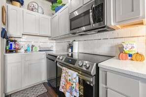 Una cucina moderna con mobili bianchi, elettrodomestici in acciaio inossidabile e zoccolo in piastrelle.