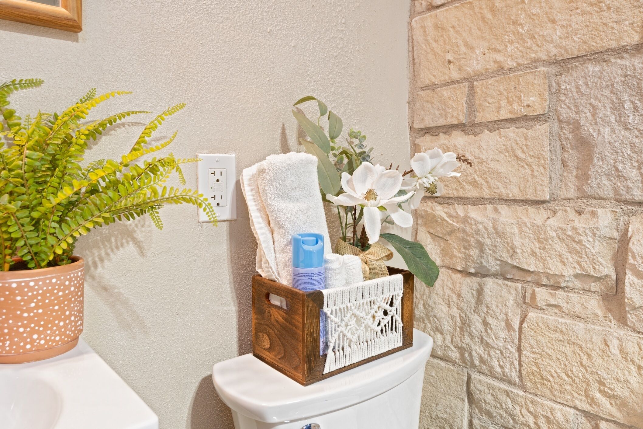 Een badkamer met een potplant, een toilet met een decoratieve mand en een stenen muur.