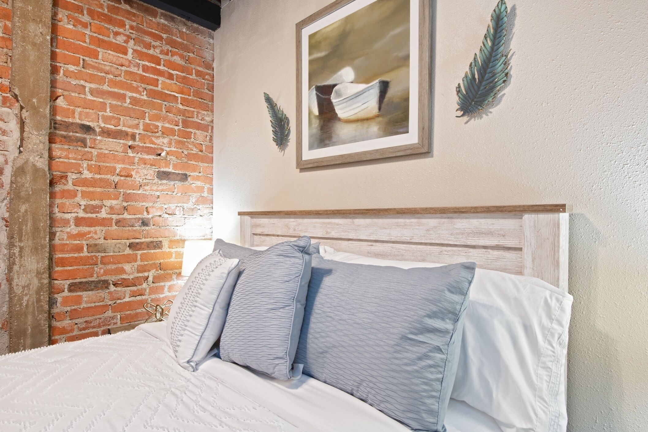 Un lit avec une literie blanche et deux oreillers, un mur en briques et un tableau encadré accroché au mur.