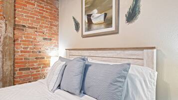 Un lit avec une literie blanche et deux oreillers, un mur en briques et un tableau encadré accroché au mur.