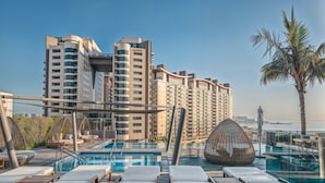 A rooftop pool area with lounge chairs and a view of high-rise buildings. - Palm Tower Palm Jumeirah By DVH Luxe (Dubai)