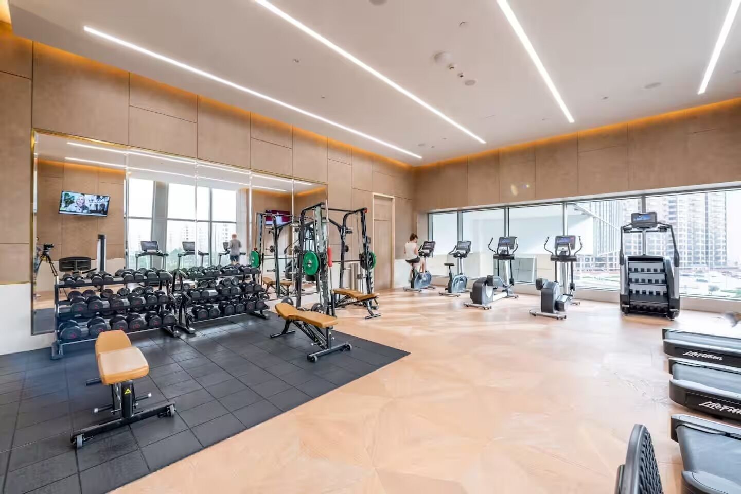 A modern gym with various exercise equipment, large windows, and a flat floor.