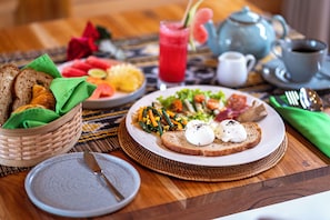 Une table dressée pour le petit-déjeuner avec des toasts, des œufs, des légumes et un panier de fruits.