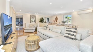 Sala moderna com televisão de tela plana, conjunto de sofás, área de jantar e vista para um cais.