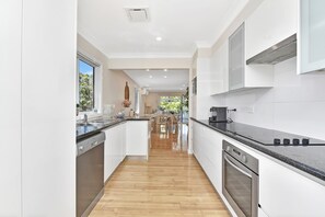 A modern kitchen with white cabinetry, a black countertop, and a wooden floor. - Upper Deck On Dobell (Wangi Wangi)