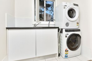 A compact laundry area with a washing machine and dryer, a window, and a sink. - Upper Deck On Dobell (Wangi Wangi)