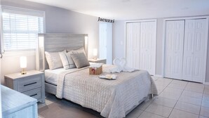 Een slaapkamer met een bed, nachtkastjes, een bedtafeltje, een raam met jaloezieën en een kledingkast.