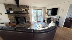 A modern living room with a stone fireplace, a large leather sofa, a flat-screen TV, and a guitar. - Fabulous 5-bedroom chalet in charming Wilmington perfect for groups (Wilmington)