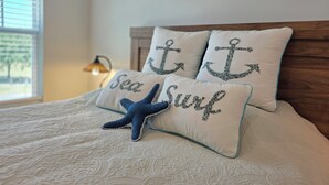 Uma cama com decoração de estrela-do-mar, dois travesseiros com desenhos de âncora e uma parede com decorações circulares de fibra.