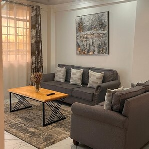 A living room with a grey sofa, a wooden coffee table, and a painting on the wall. - Koselig Homes califonia Plaza Nanyuki (Nanyuki)