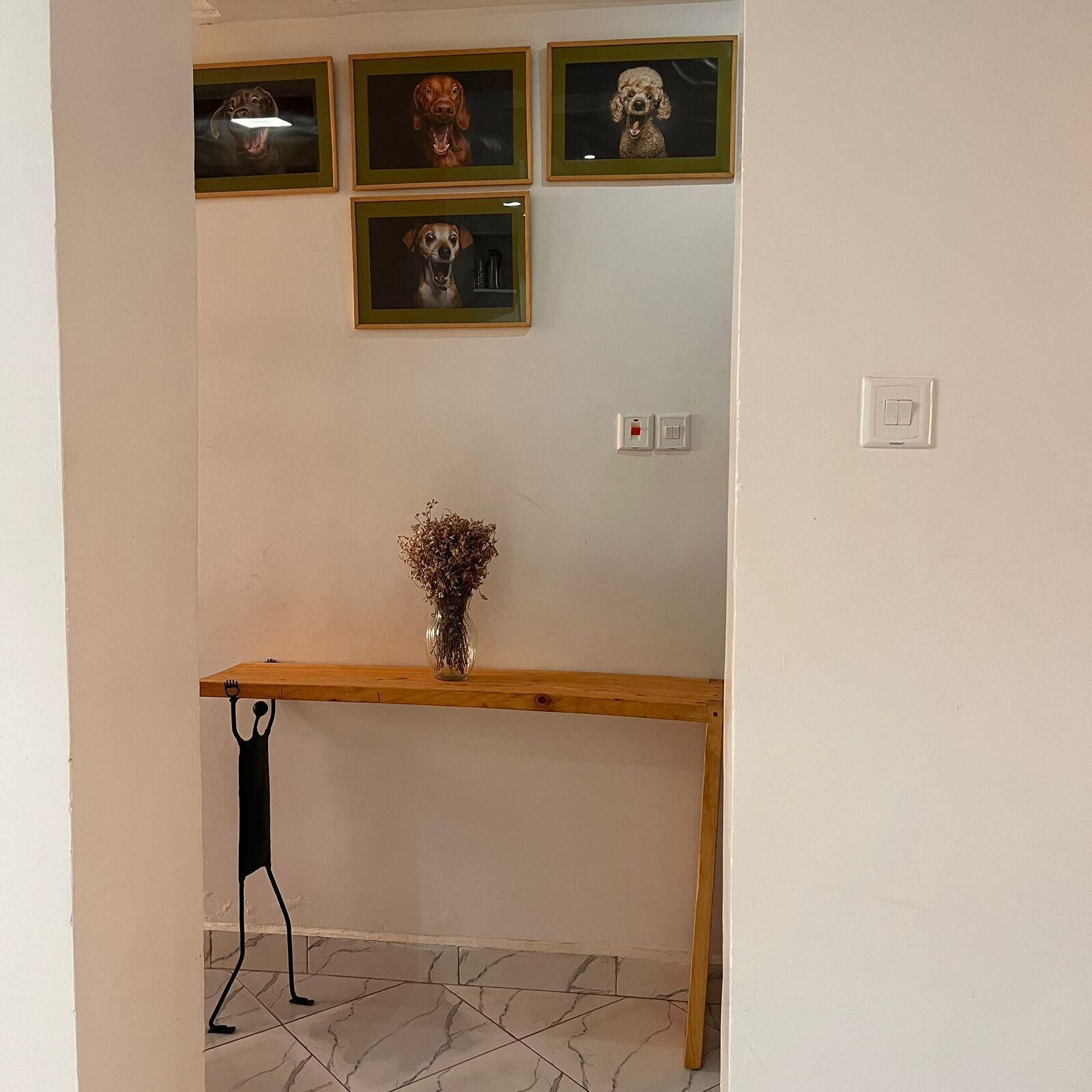 A room with a wooden console table, a vase with dried flowers, and framed pictures on the wall.
