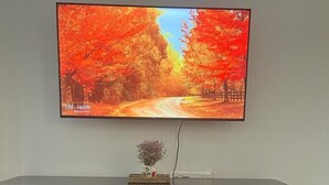 Una televisione montata a parete sopra un mobile intrattenimento nero con un telecomando su un tavolo di fronte.