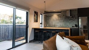 Een moderne keuken met een groot eiland, barstoelen en een glazen schuifdeur naar een buitenruimte.